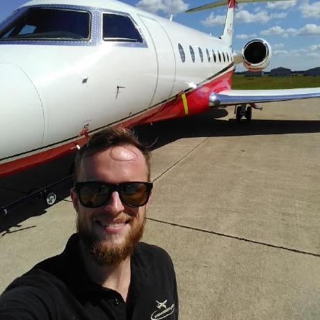 TJ in sunglasses, smiling on an airport ramp in front of a white business jet with a red stripe.